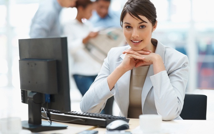 Pretty Caucasian business woman at office desk with colleagues in the back